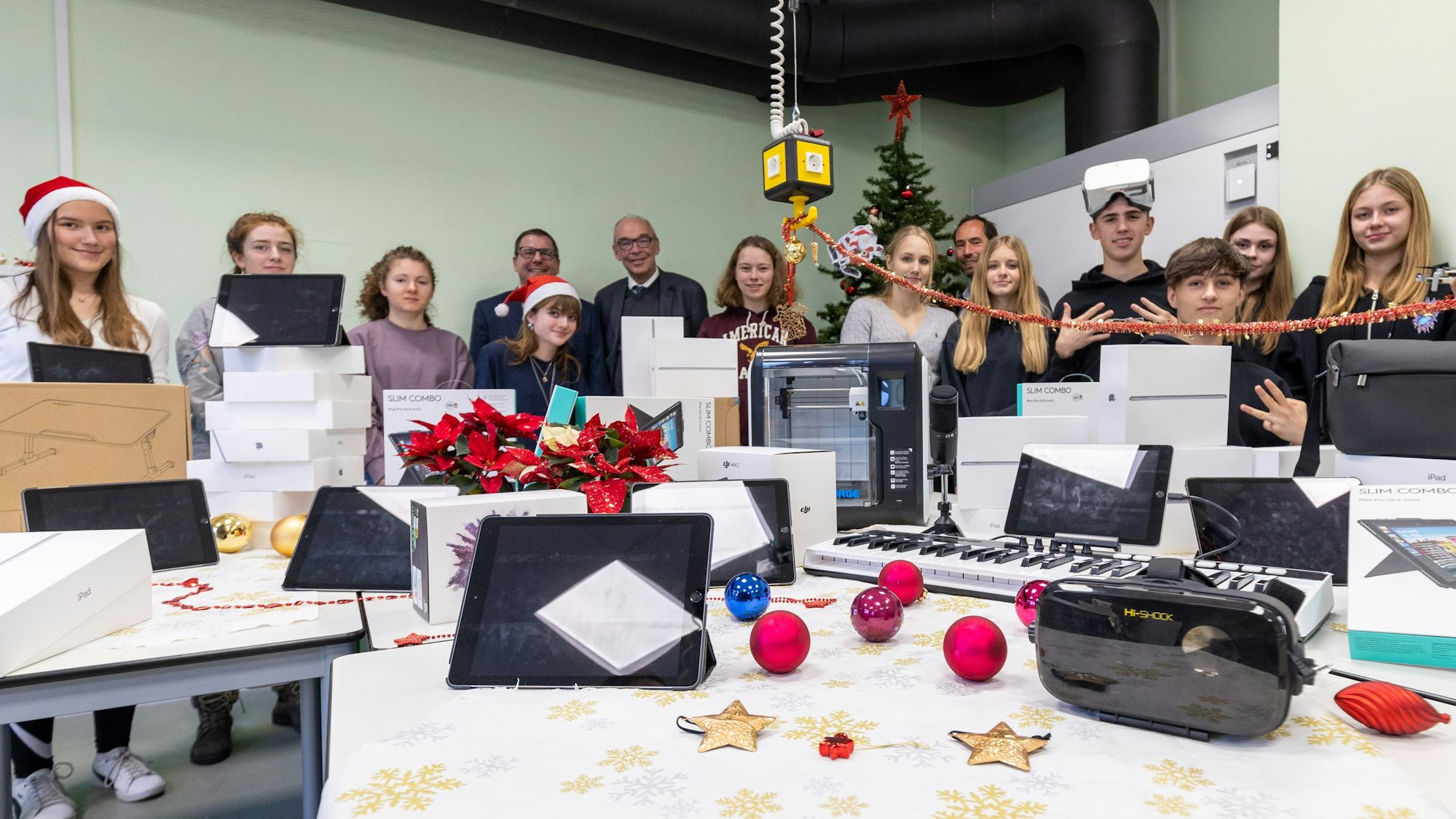 Zahlreiche Digitalgeräte vom Tablet bis zum 3D-Drucker oder dem Tonstudio liegen auf einem weihnachtlich dekorierten Tisch, Schüler, Schulleiter und Vertreter der Stadt stehen dahinter.