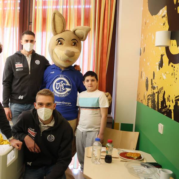 Die Handballspieler Tom Kiesler, Stepan Zeman und Tom Jansen posieren mit dem lebensgroßen VfL-Maskottchen, dem Känguru Gummi und dem zehn Jahre alten Ben für ein Gruppenfoto in einem Krankenzimmer der Kinderklinik.