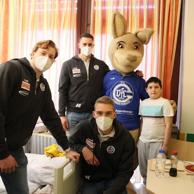 Die Handballspieler Tom Kiesler, Stepan Zeman und Tom Jansen posieren mit dem lebensgroßen VfL-Maskottchen, dem Känguru Gummi und dem zehn Jahre alten Ben für ein Gruppenfoto in einem Krankenzimmer der Kinderklinik.