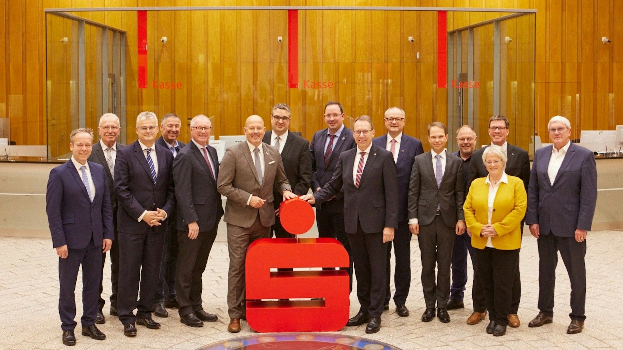 Angestellte der Sparkassen aus Köln und Radevormwald/Hückeswagen stehen in der Hauptstelle der Kreissparkasse Köln vor einem Sparkassen-Logo