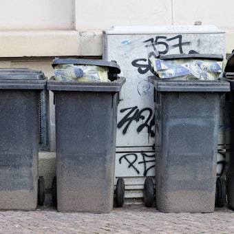 Volle Mülltonnen stehen an einer Hauswand.