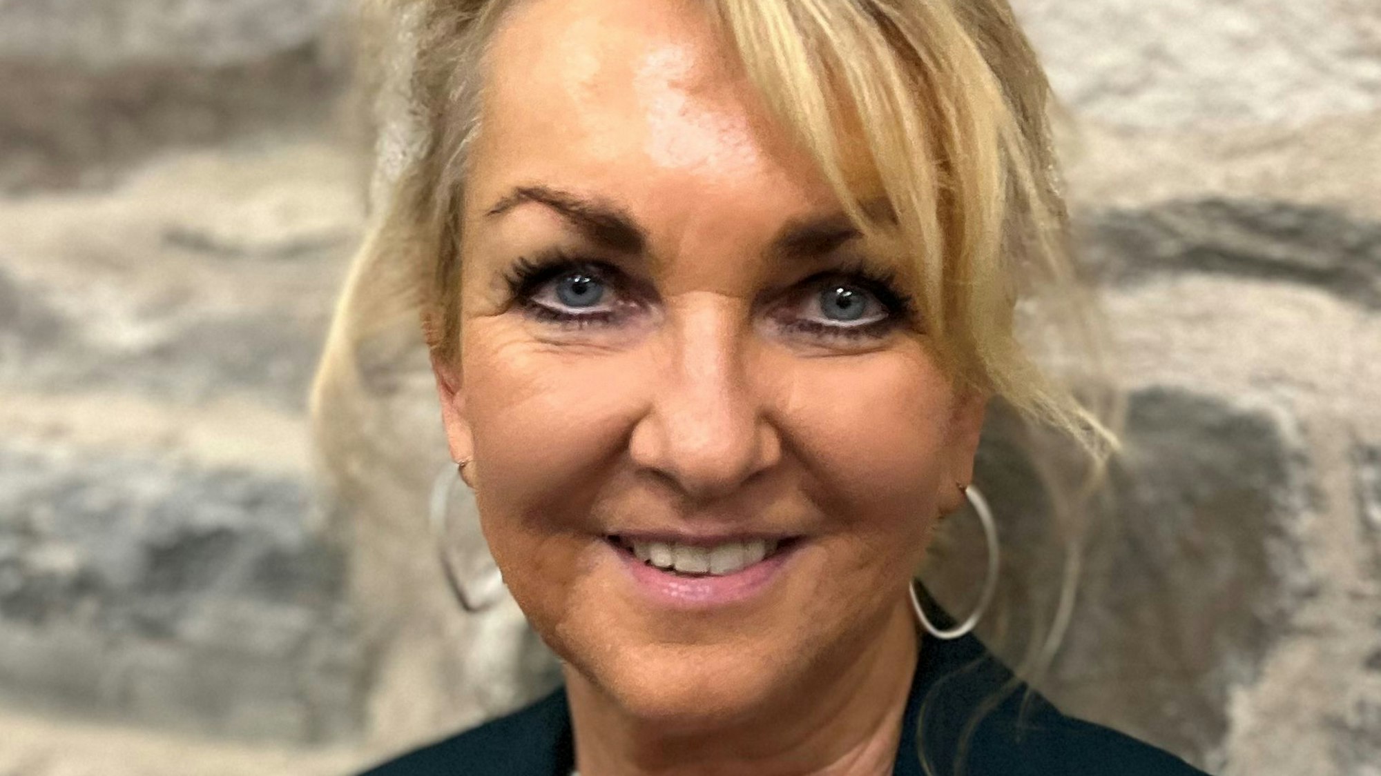 Gabi Wilhelm, die neue Geschäftsführerin der Naturarena Bergisches Land GmbH, steht vor einer Bruchsteinwand.