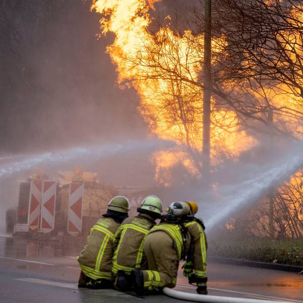Feuerwehrleute arbeiten daran, das brennende Gasleck in Duisburg zu löschen. Ein Feuer und Rauchschwaden sind zu sehen, im Vordergrund die Feuerwehrleute.