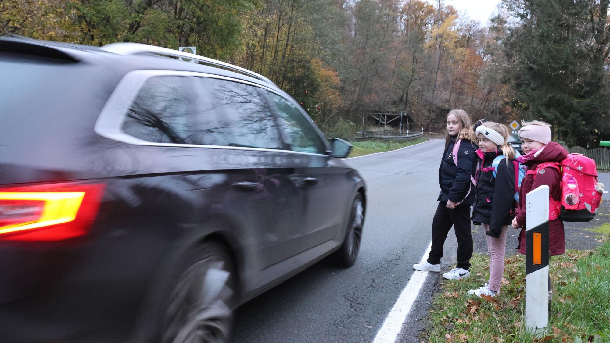 Drei Schulkinder stehen am Rand der L 320. Diese viel befahrene Straße müssen sie auf dem Weg zum Schulbus überqueren.