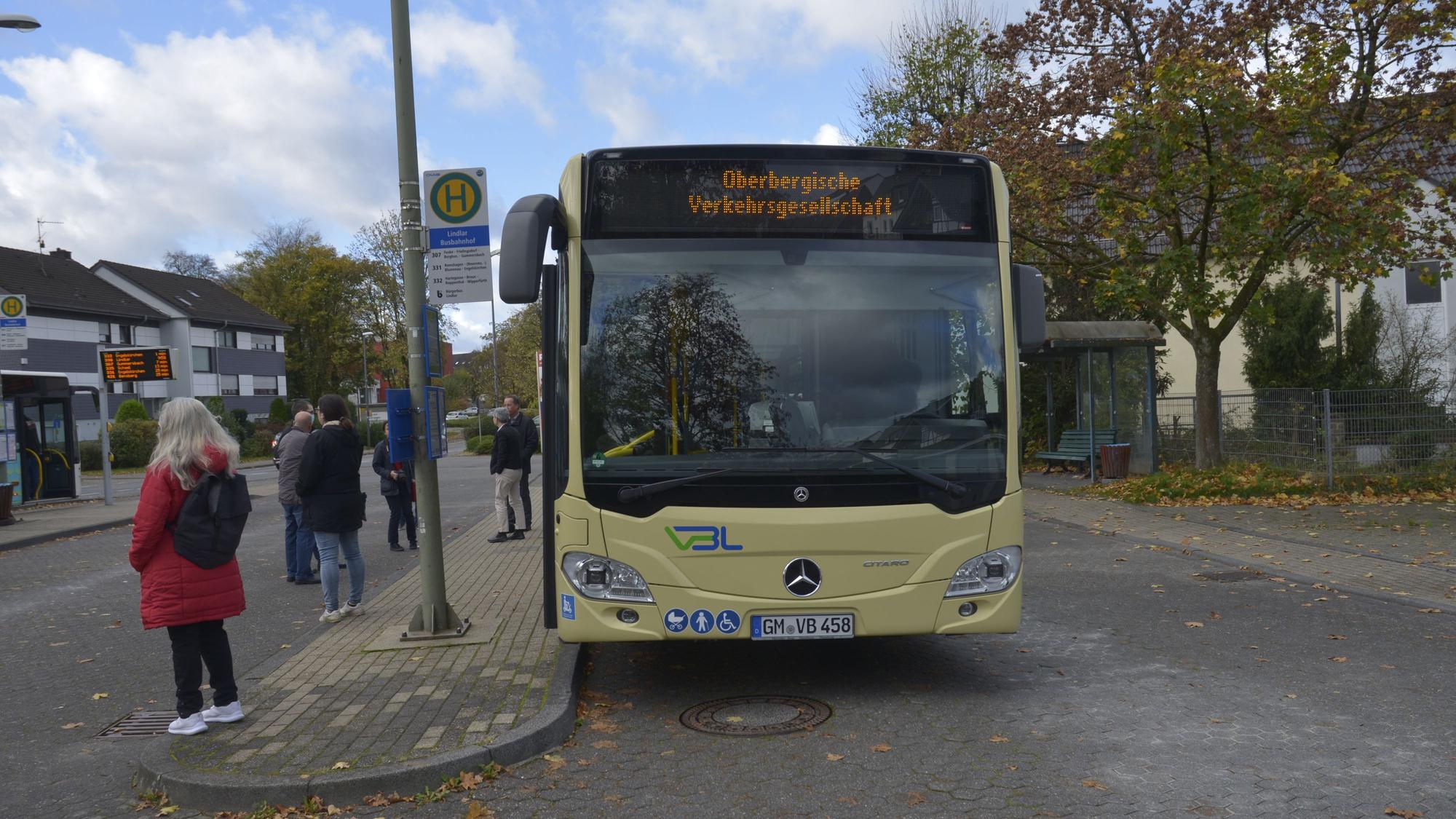 Ein Bus und mehrere Personen warten an einer Haltestelle.