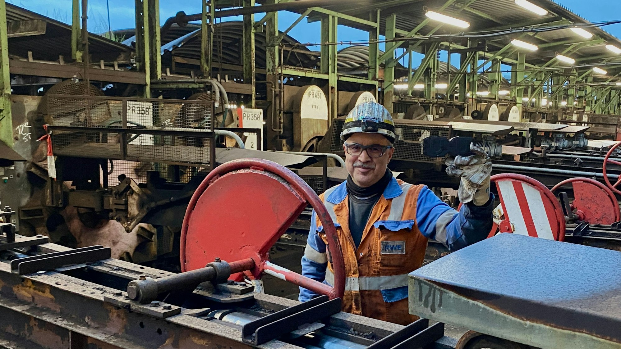 Ein Mann in Warnweste und mit Sicherheitshelm steht an einer Maschine der Brikettfabrik am Wachtberg.