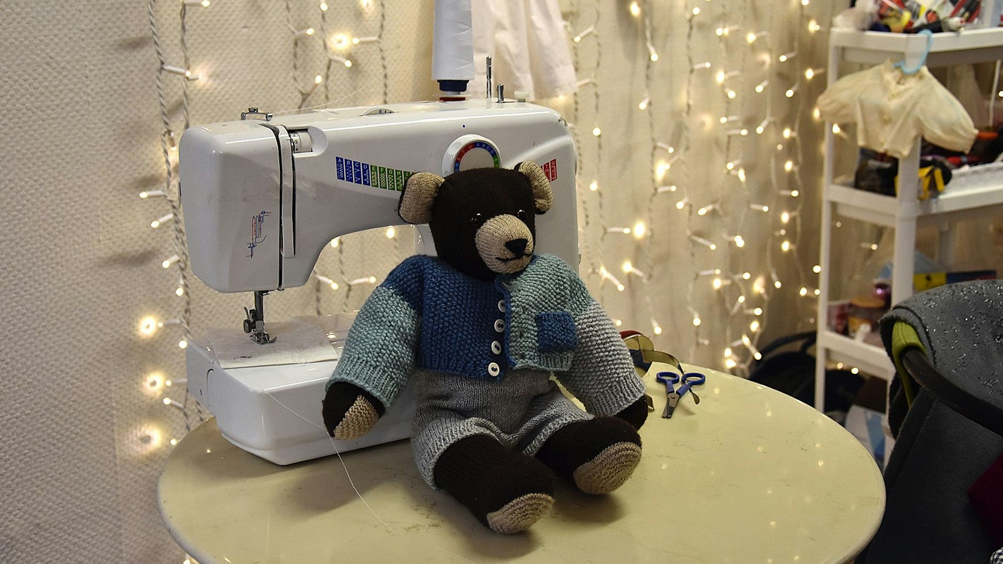 Vor einer Nähmaschine sitzt ein Stoffteddybär, dem ein Auge fehlt.