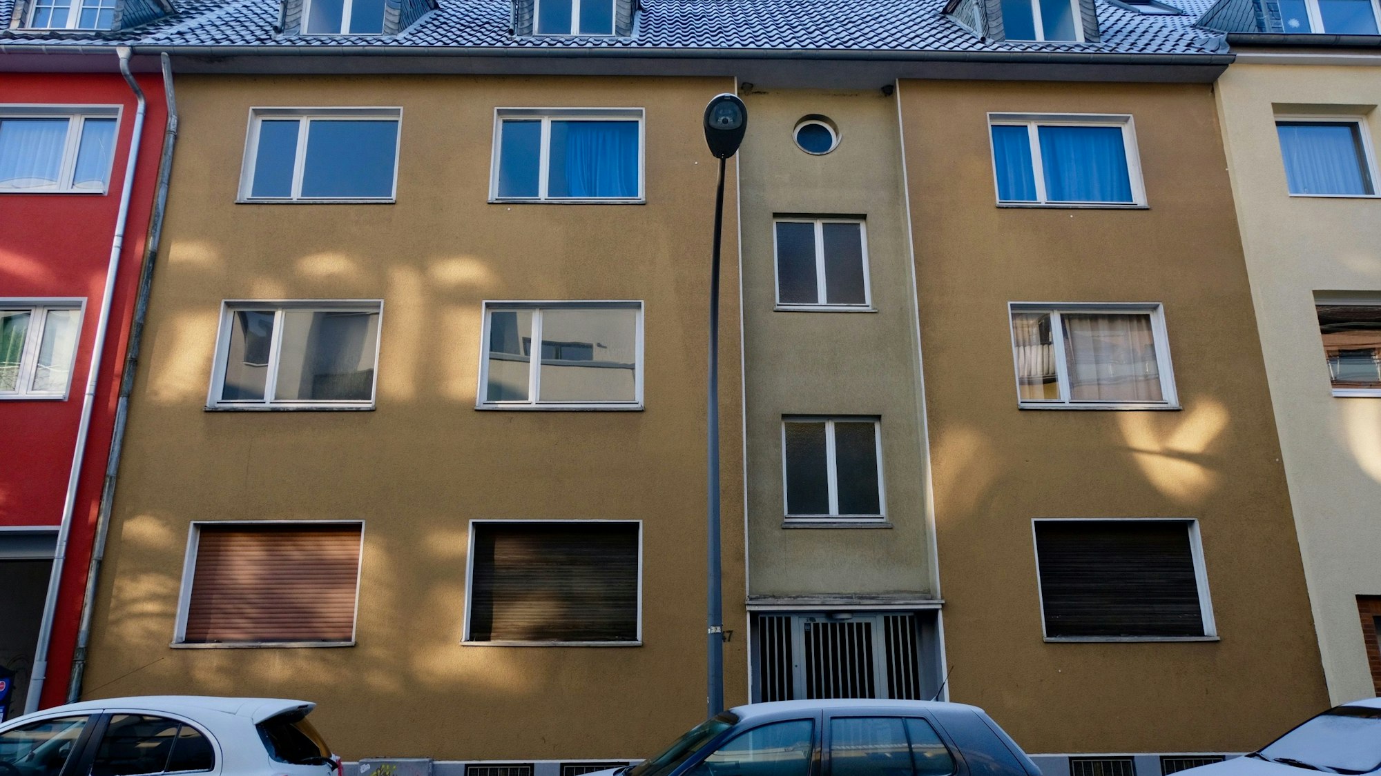 Ein vierstöckiges Wohnhaus mit brauner Fassade ist zu sehen. Davor parken Autos.
