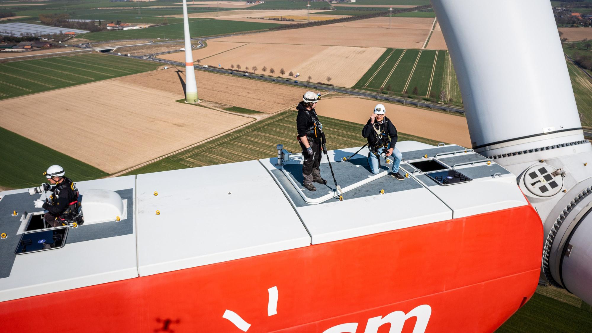 Personen stehen auf einem Windrad. In NRW soll die Abstandsregel für Windräder zu Siedlungen fallen. (Symbolbild)