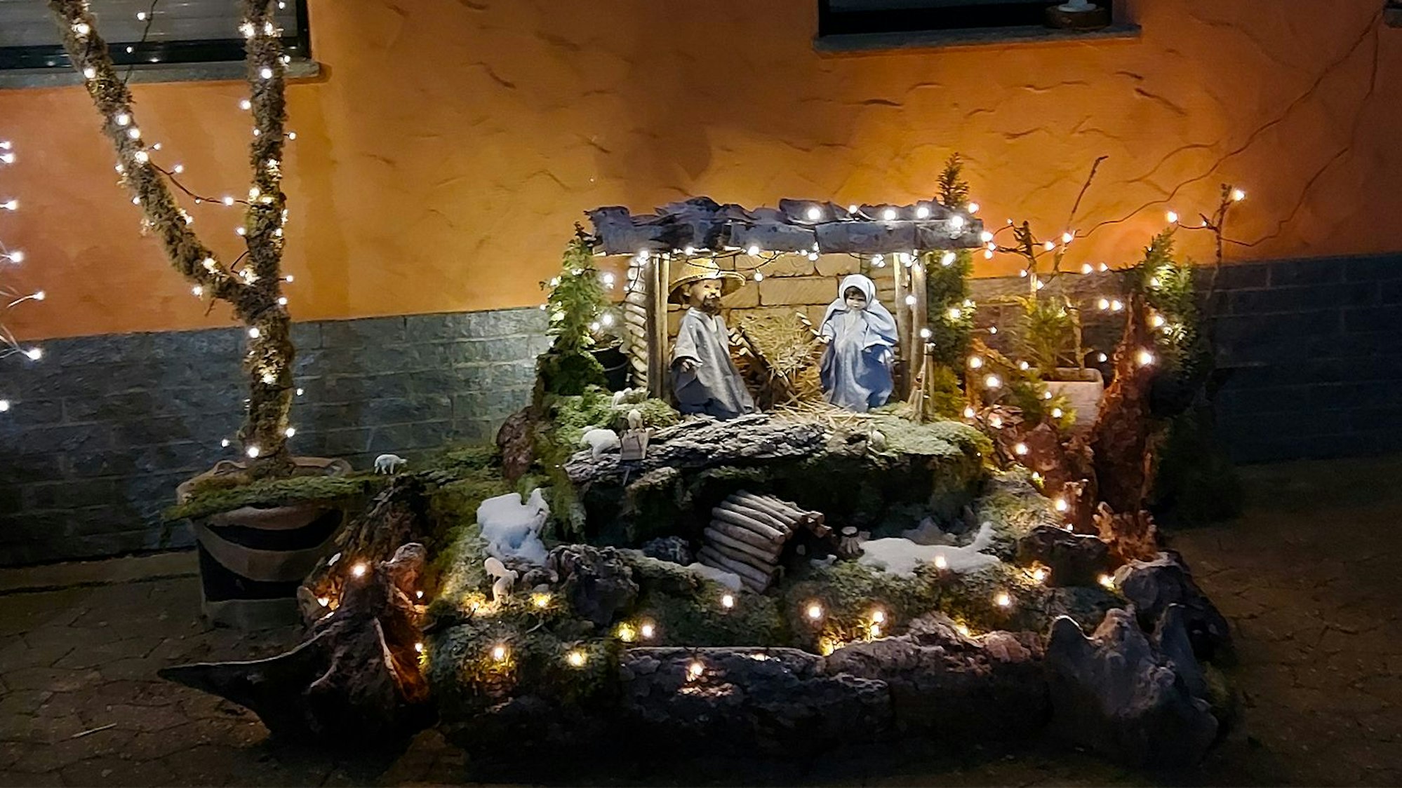 Eine beleuchtete Krippe steht vor einer Hauswand.