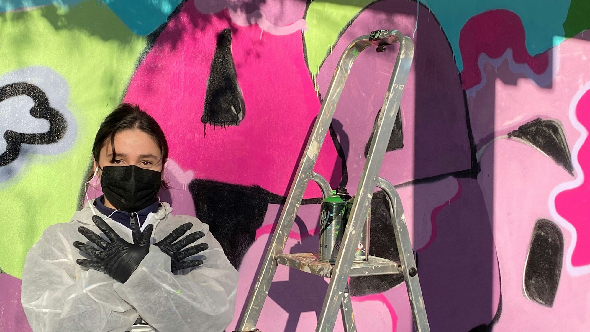 Eine Schülerin an der Gesamtschule Swisttal formt vor einem Friedens-Graffiti mit ihren Händen in schwarzen Schutzhandschuhen eine Friedenstaube.