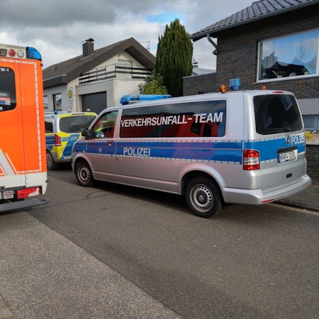 Ein Notarztwagen und Polizeiautos stehen vor einem Haus.