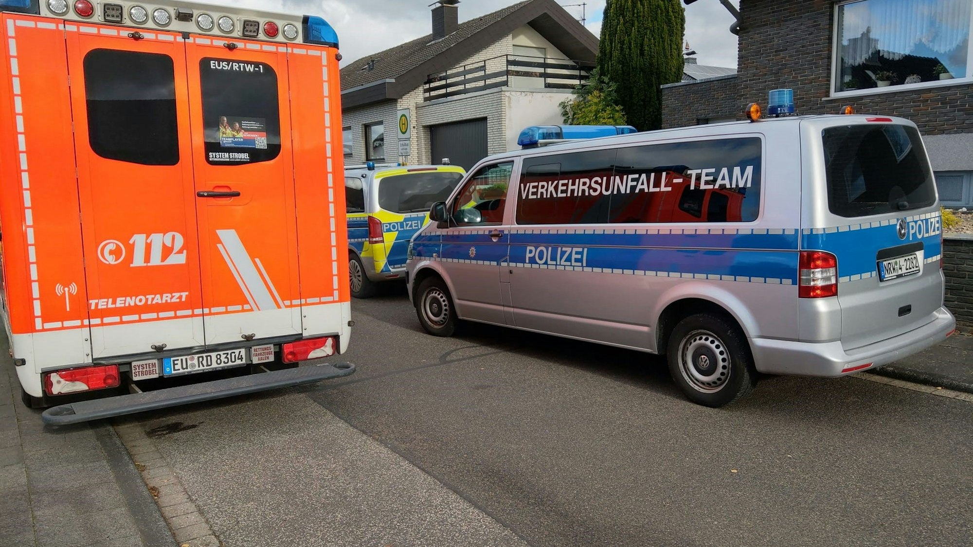 Ein Notarztwagen und Polizeiautos stehen vor einem Haus.