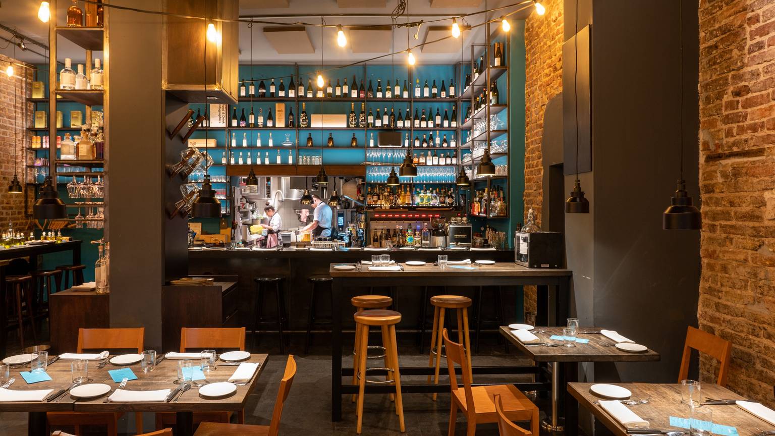 Innenraum eines Restaurants mit Holzstühlen und -tischen, im Hintergrund eine Bar