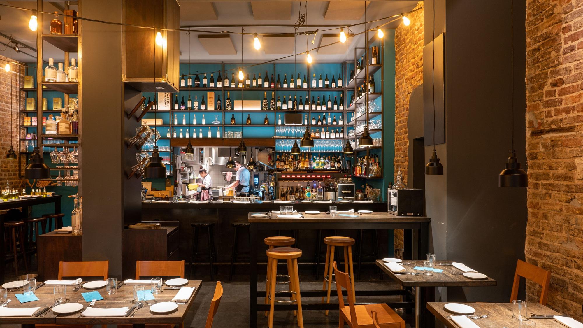 Innenraum eines Restaurants mit Holzstühlen und -tischen, im Hintergrund eine Bar