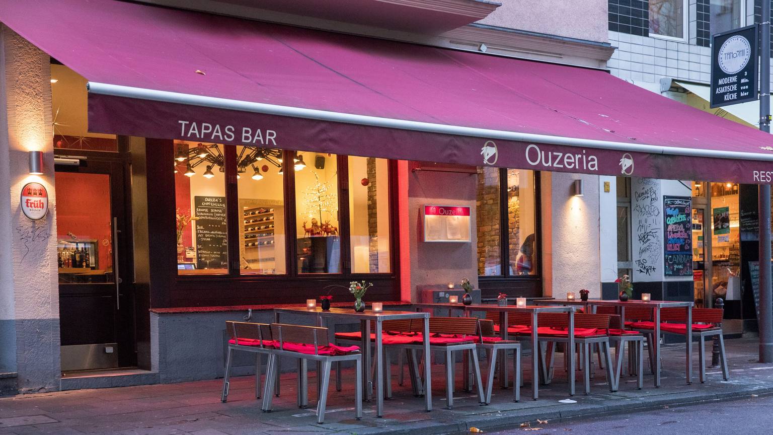 Restaurant von außen mit roter Markise über Tischen und Stühlen