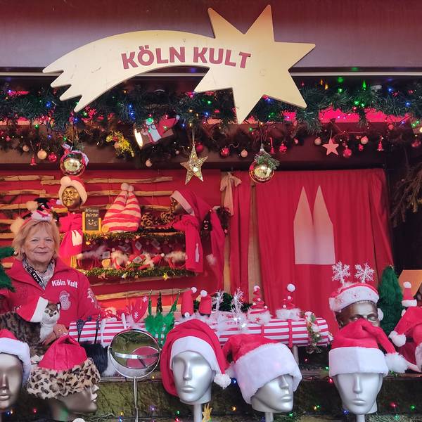 Eine Frau steht in einer Bude, in der es Weihnachtsmützen zu kaufen gibt.