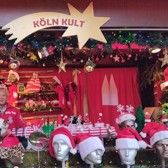 Eine Frau steht in einer Bude, in der es Weihnachtsmützen zu kaufen gibt.