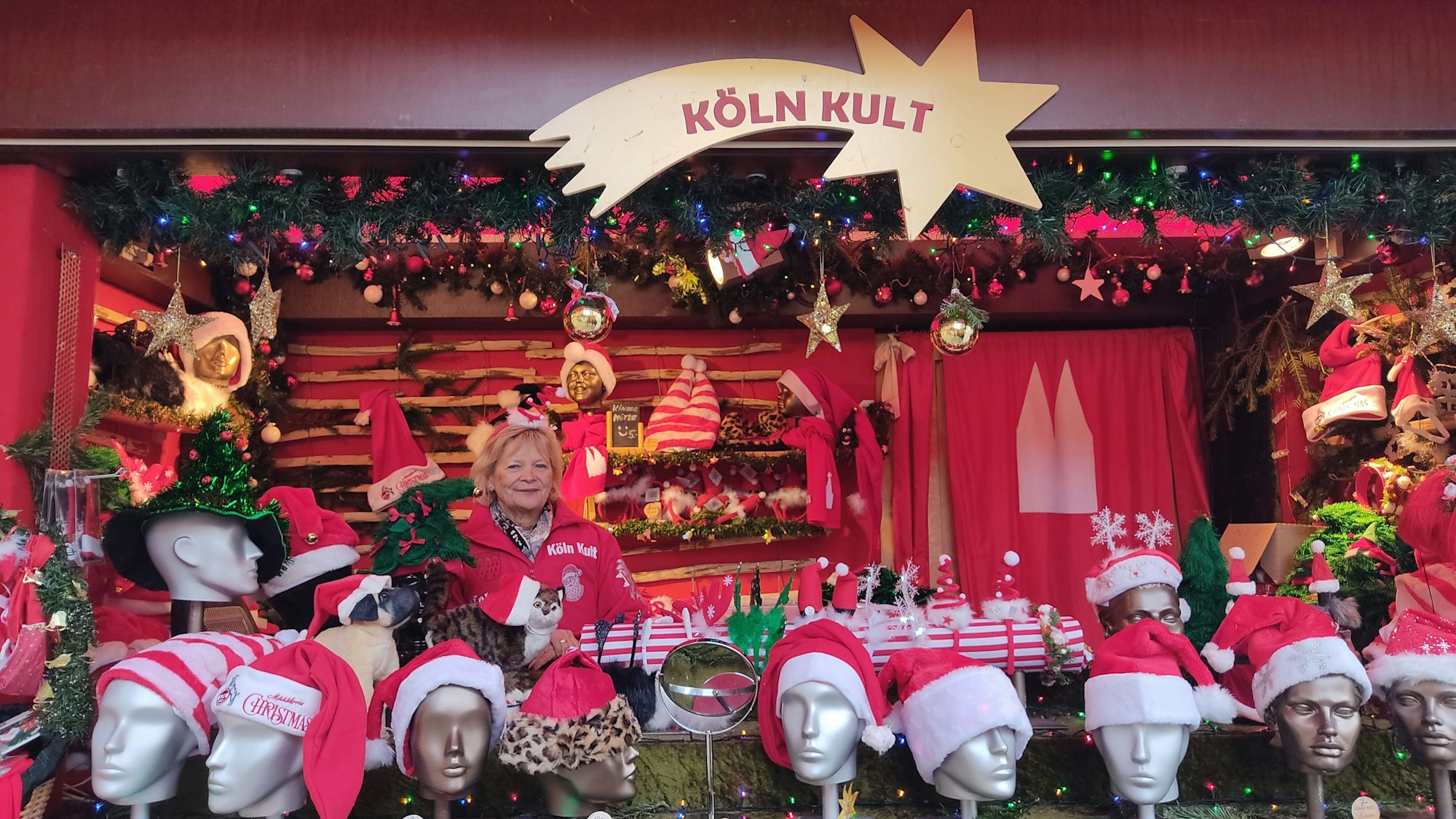 Eine Frau steht in einer Bude, in der es Weihnachtsmützen zu kaufen gibt.