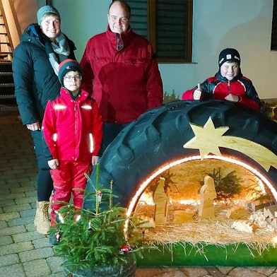 In einem Traktorreifen ist die Krippenszene integriert. Dahinter steht die Familie, die diese Krippe gebaut hat.