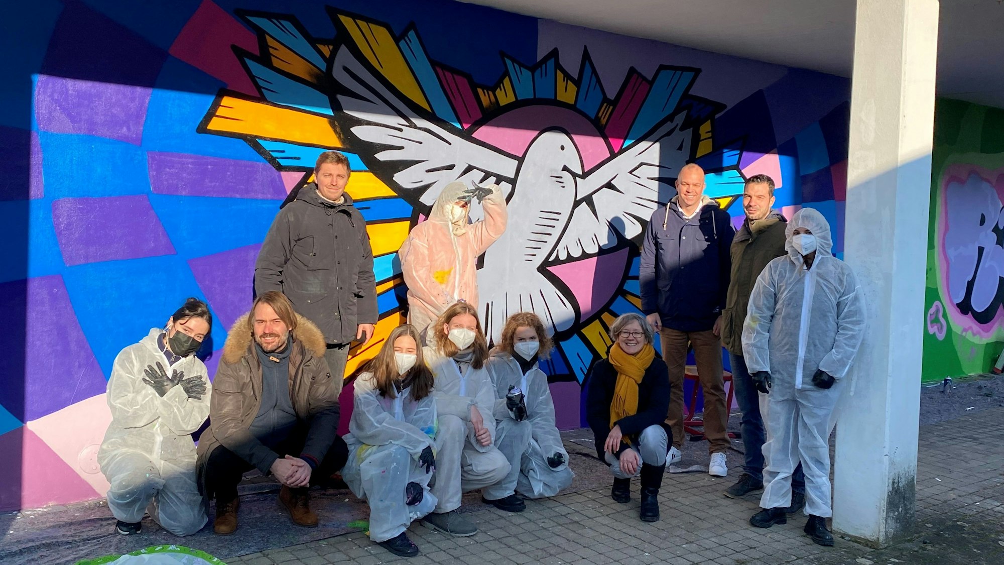 Schüler in Schutzanzügen zeigen sich vor dem fertigen Kunstwerk, das eine Friedenstaube darstellt.