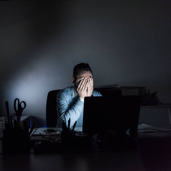 Ein Mann sitzt in einem dunklen Büro am Computer und hält sich die Hände vors Gesicht.