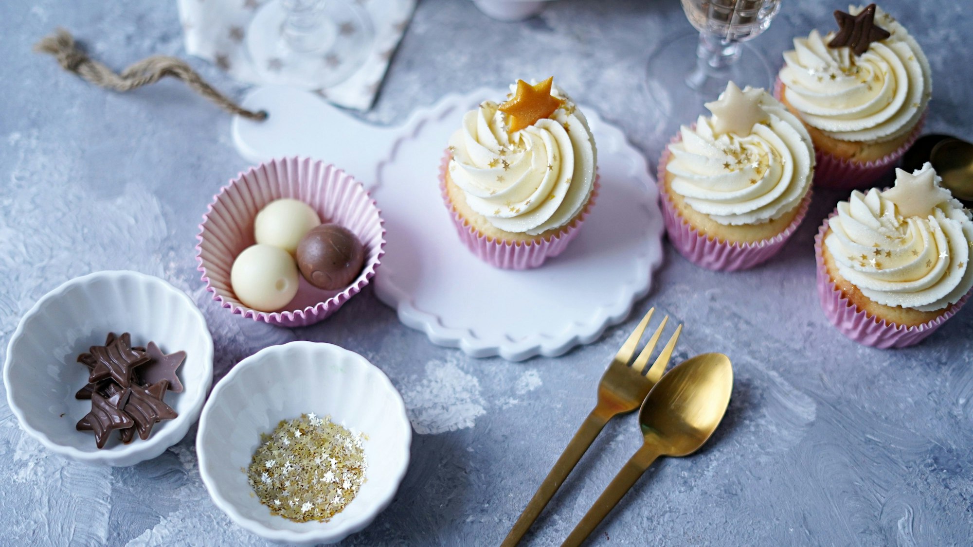 Die Cupcakes stehen verziert in pinken Förmchen auf einem weihnachtlich gedeckten Tisch.
