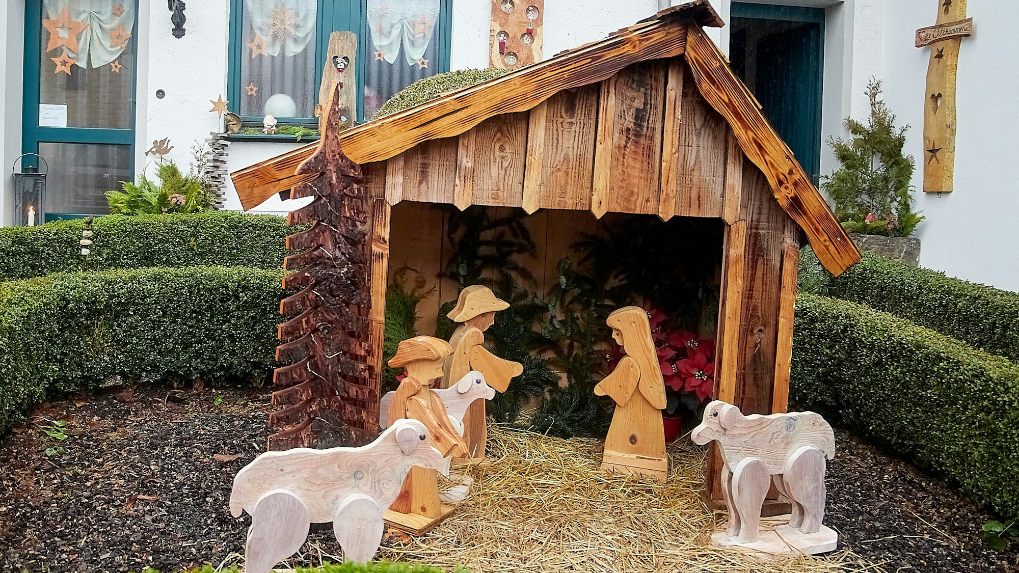 Eine Krippe mit Holzfiguren steht vor einem Wohnhaus.