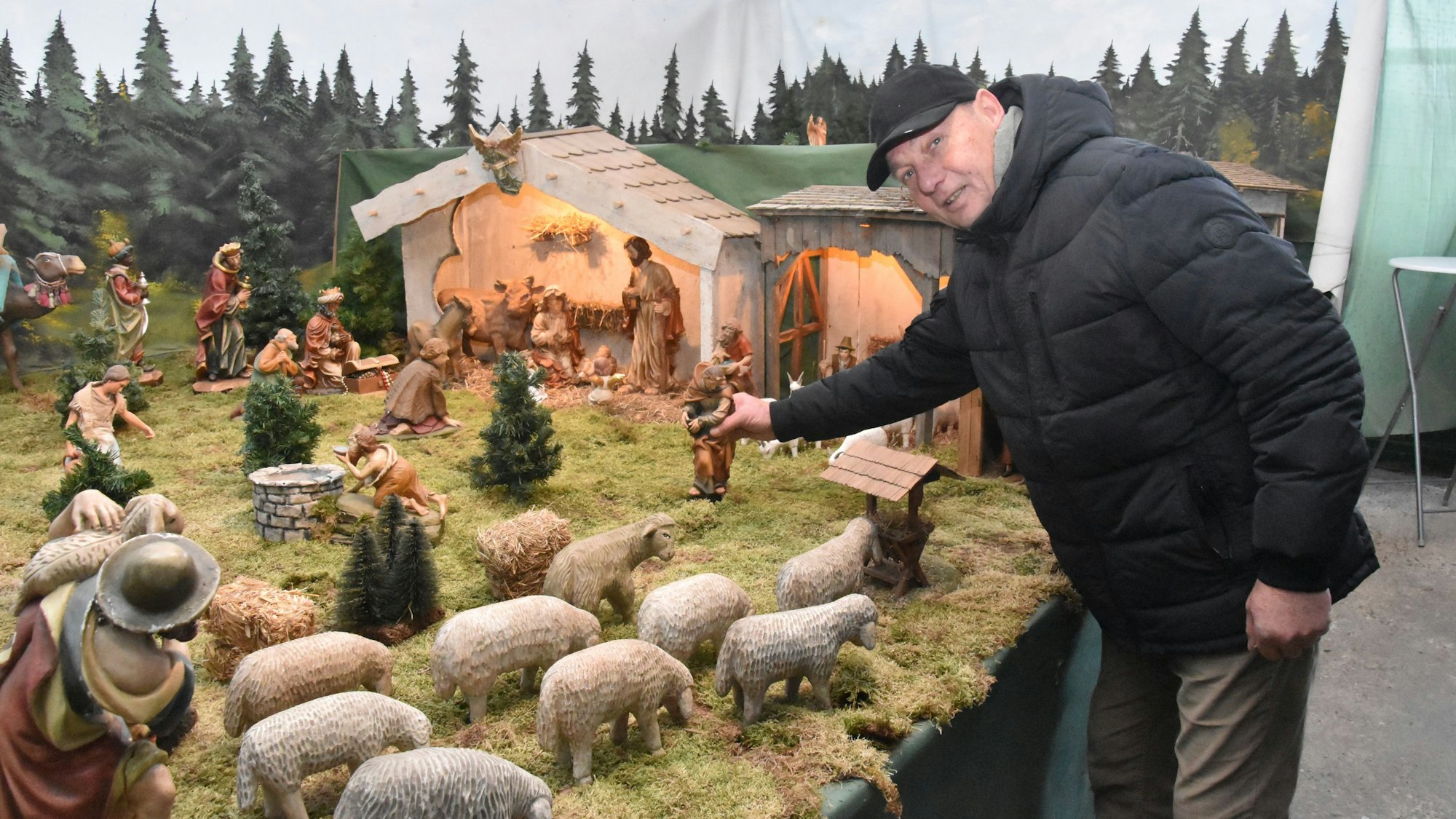 Ein Mann stellt eine Figur in eine Krippenlandschaft.