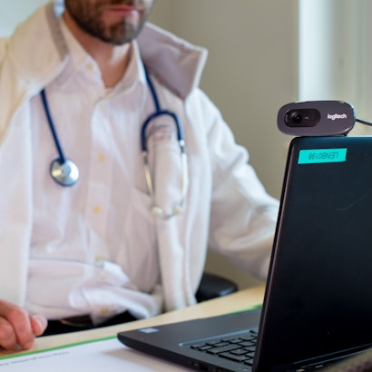 Ein Hausarzt spricht während einer Videosprechstunde in seiner Praxis mit einer Patientin.