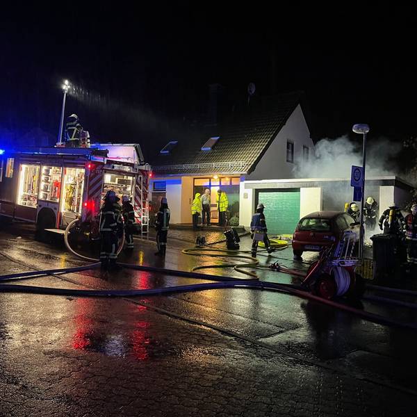 Feuerwehrleute stehen vor einer Garage in Lindlar, aus der Rauch dringt.
