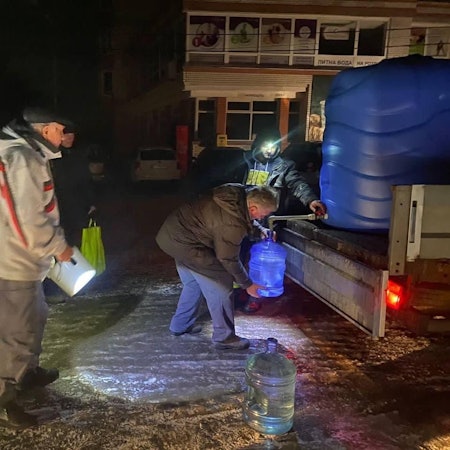Menschen mit Eimern füllen Wasser an einem großen Tank von der Ladefläche eines Kleinlasters ab.