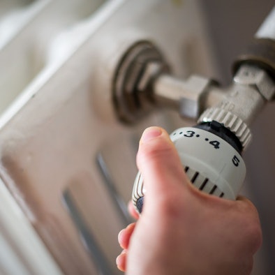 Eine Hand reguliert die Temperatur an einer Heizung.