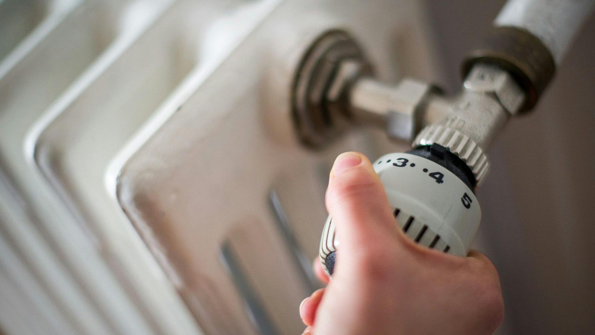 Eine Hand reguliert die Temperatur an einer Heizung.