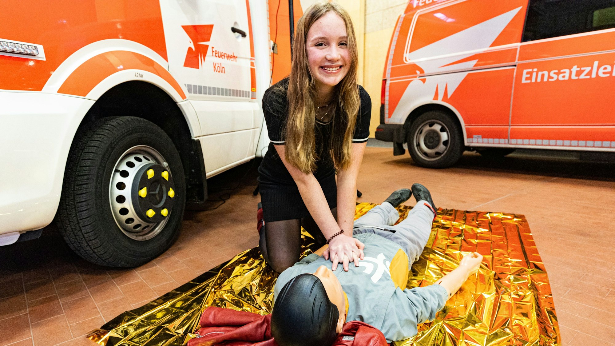 Valerie Grässler demonstriert ihre Wiederbelebungs-Fertigkeiten an einer Puppe. Im Hintergrund stehen zwei Fahrzeuge der Feuerwehr.
