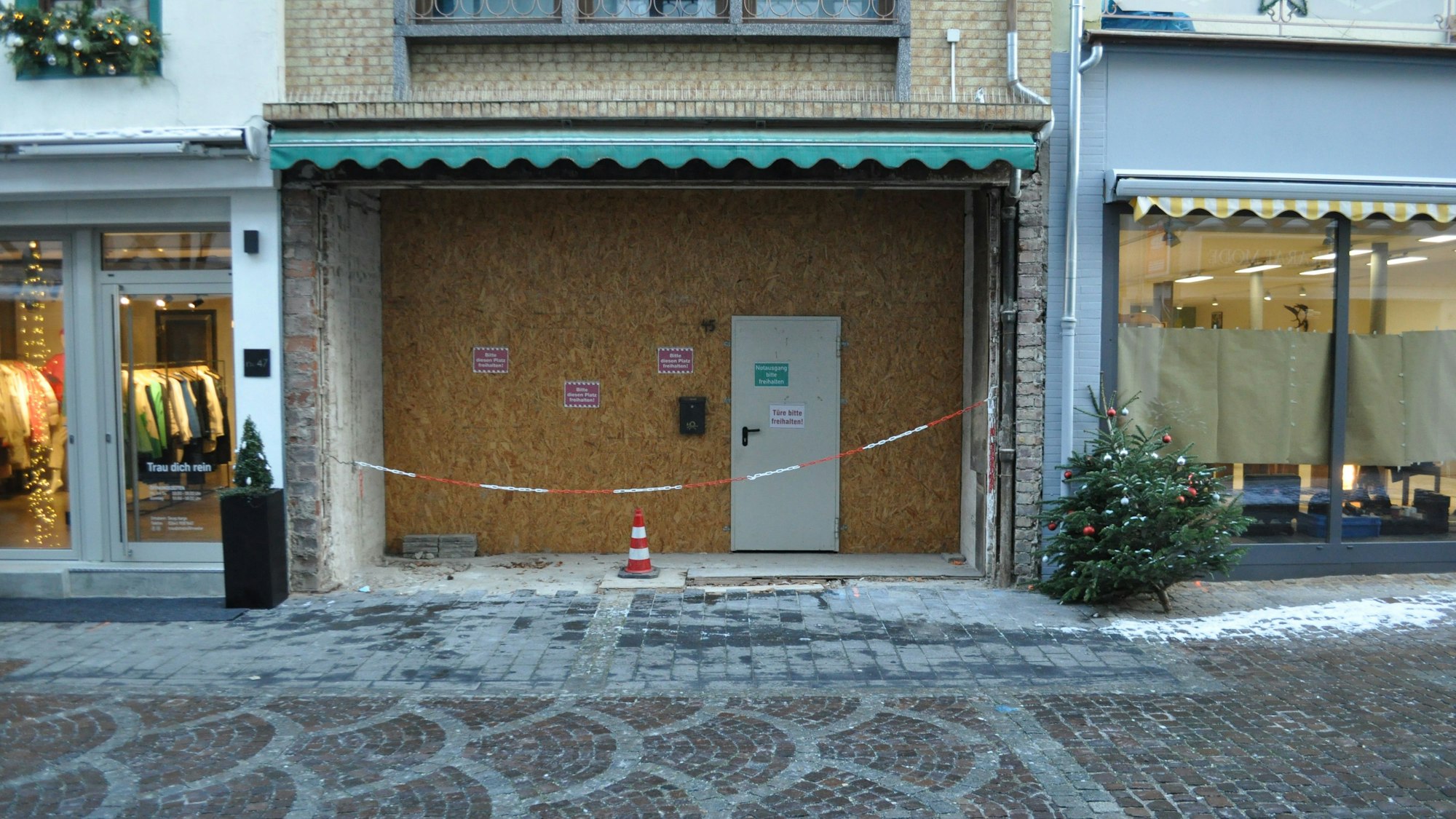 Ein Weihnachtsbaum steht neben einer verrammelten Ladenfront.