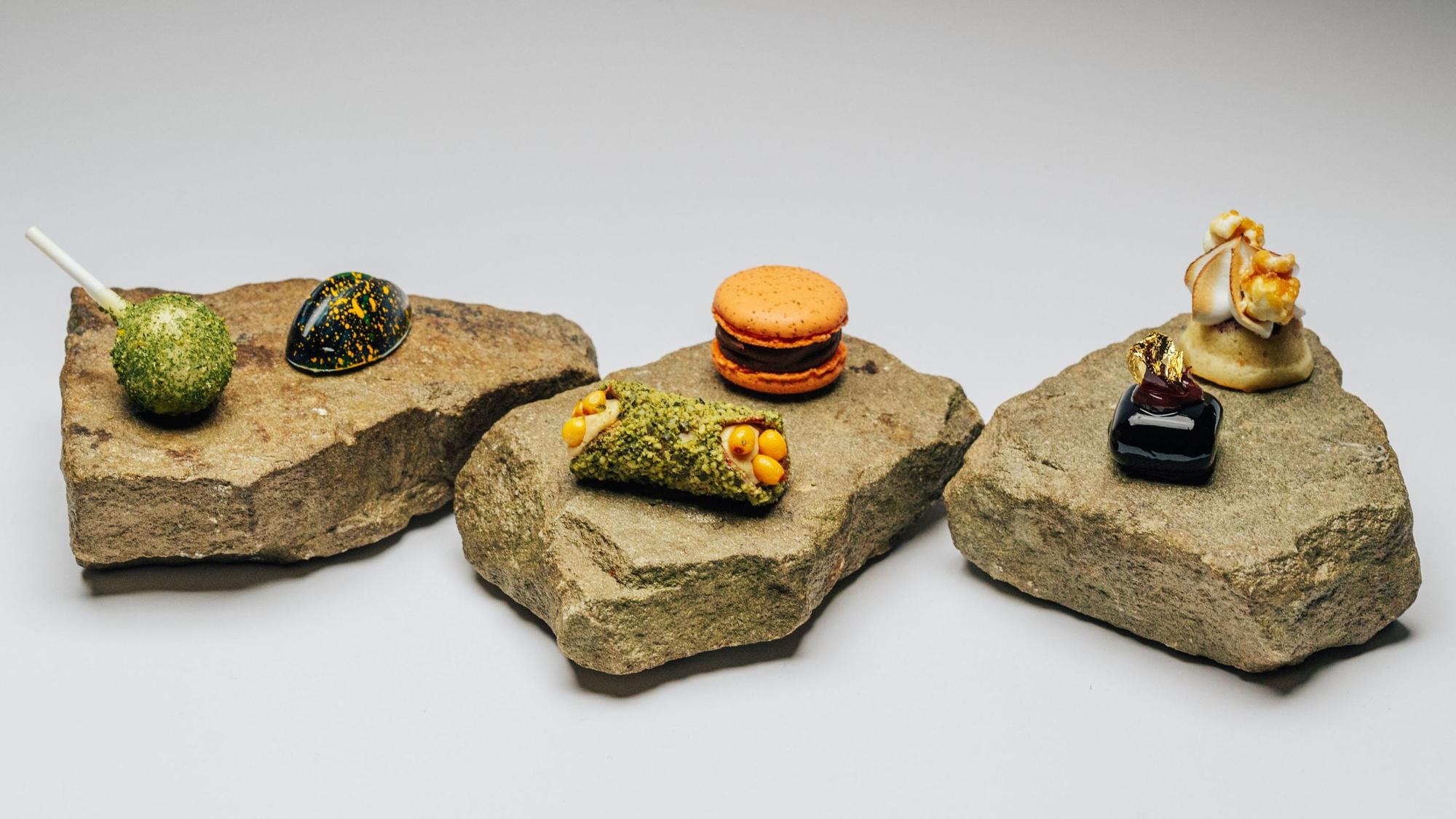 Sechs kleine Desserts werden im Ox & Klee in Köln auf drei Steinplatten serviert. Dabei ist unter anderem eine Art grüner Lolli, eine schwarze Praline mit orangenen Sprenkeln oder ein orangene Macaron.