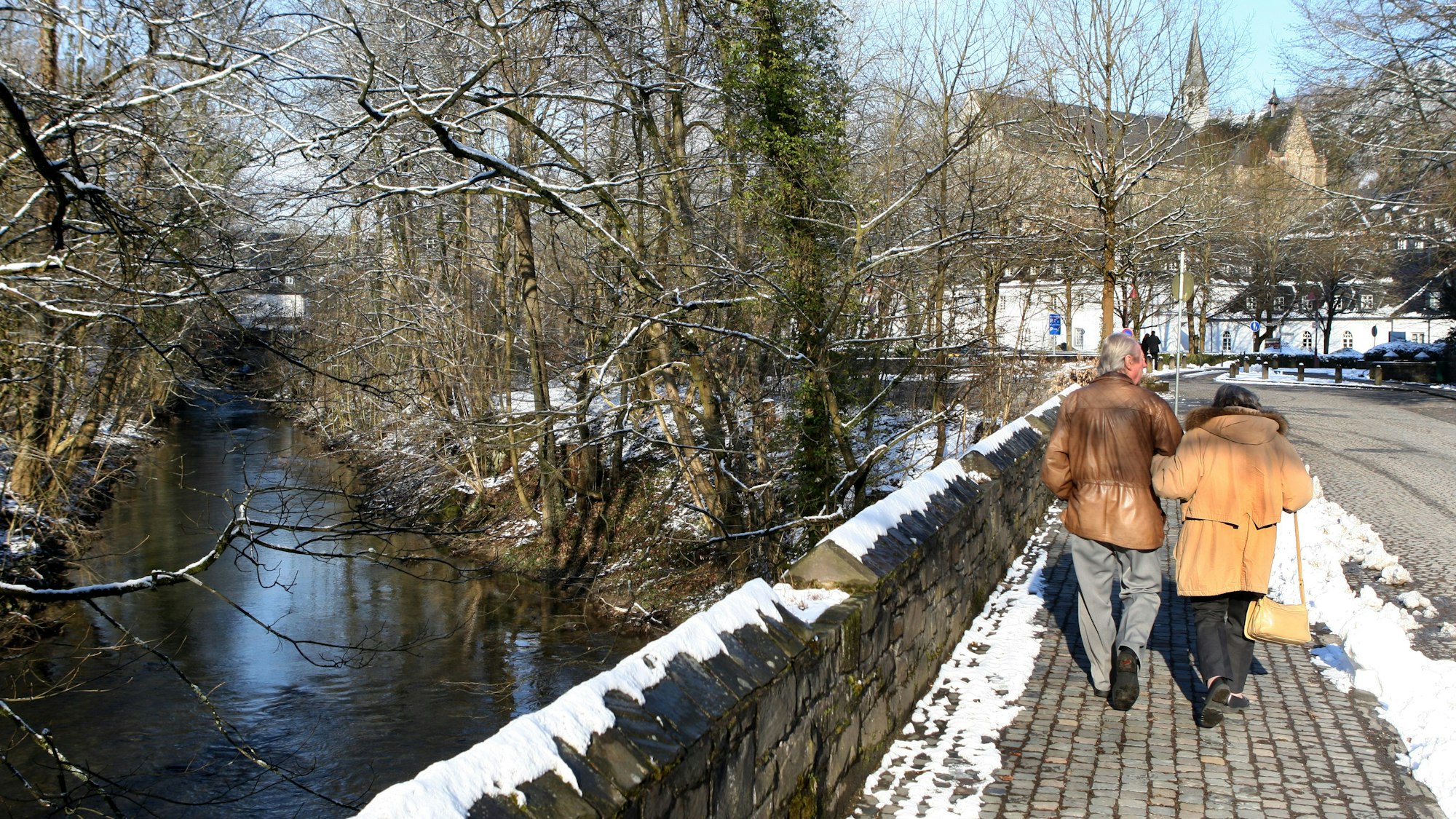 Zwei Menschen gehen über die Dhünnbrücke auf den Altenberger Dom zu.