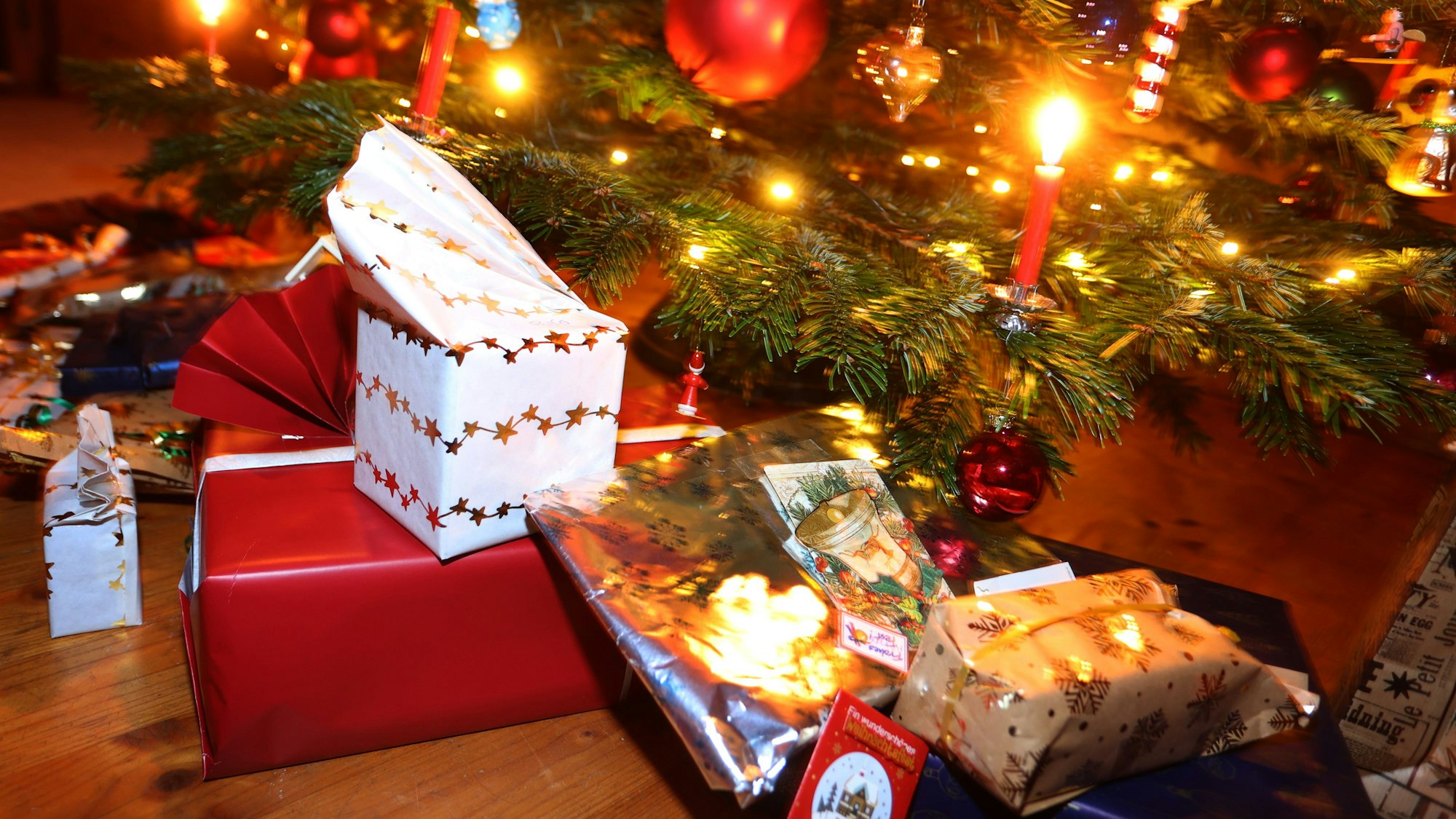 Man sieht den Fuß eines geschmückten Weihnachtsbaum, darunter liegen eingepackte Geschenke.