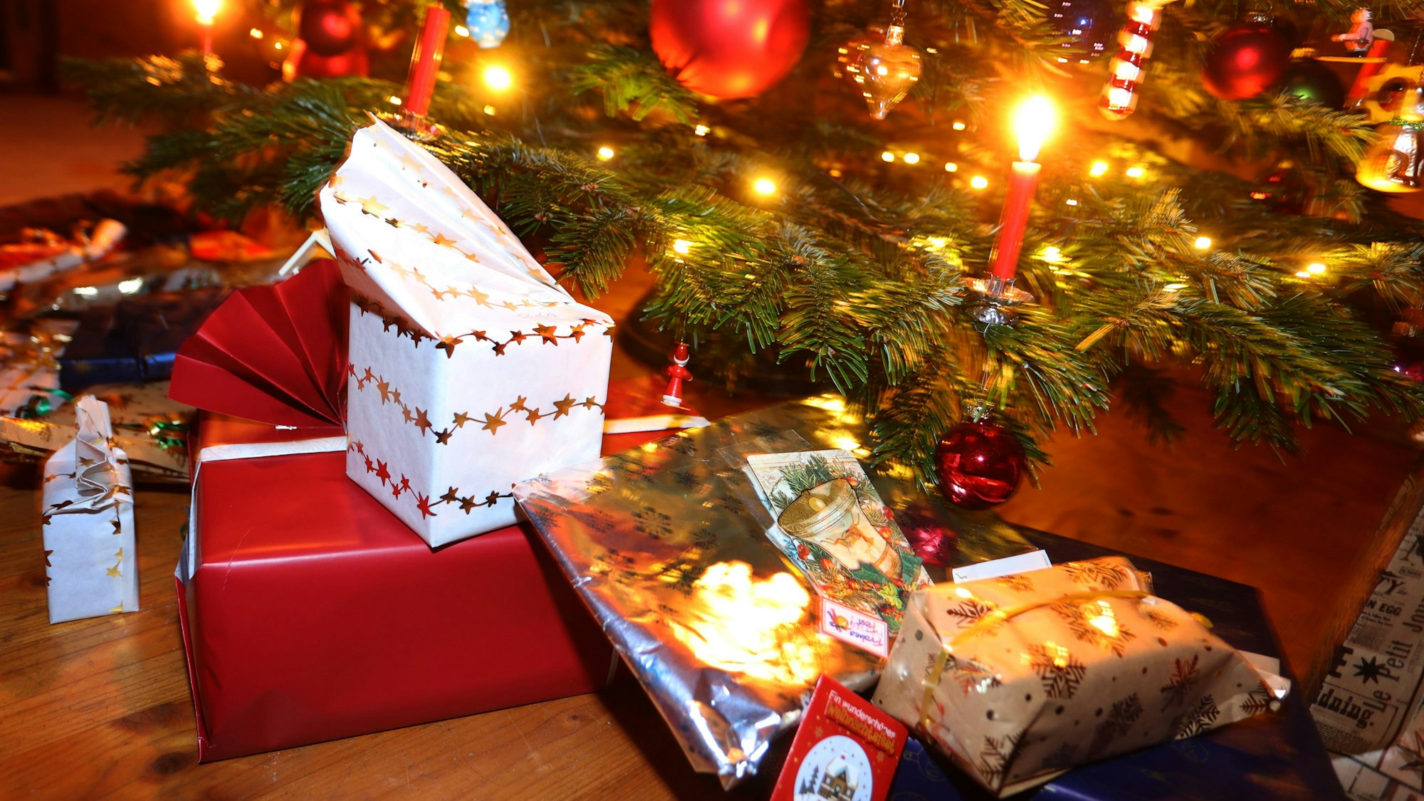 Man sieht den Fuß eines geschmückten Weihnachtsbaum, darunter liegen eingepackte Geschenke.