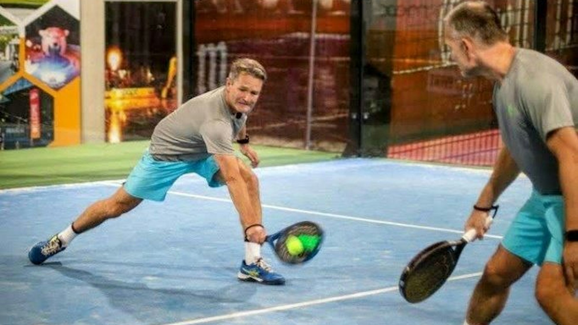 Zwei Männer spielen auf einem Feld Padel mit Schlägern.