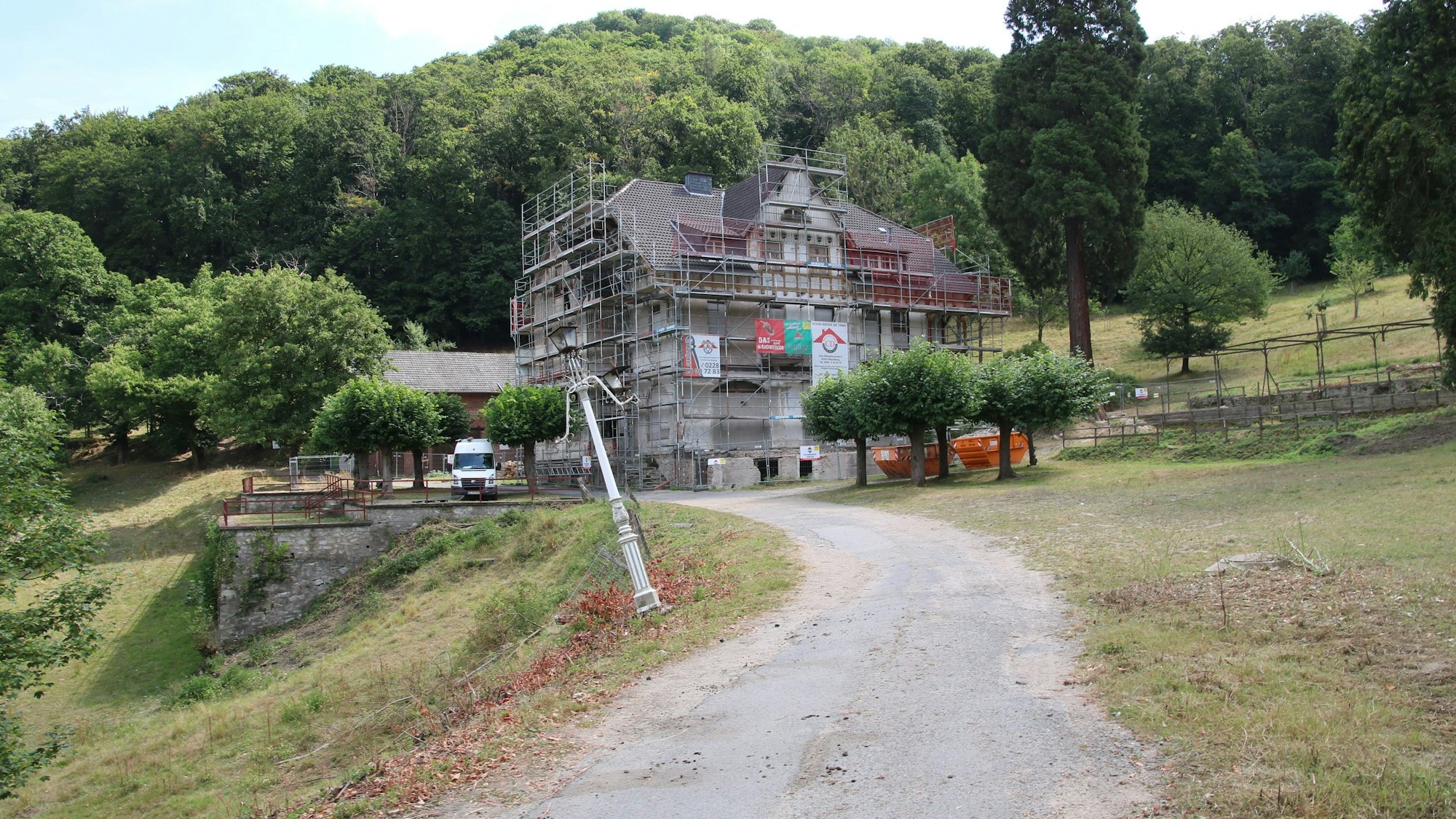Am Ende eines Weges steht ein komplett eingerüstetes Gebäude, davor ein weißer Transporter. Im Vordergrund ist eine halb umgeknickte alte Straßenlaterne zu sehen.