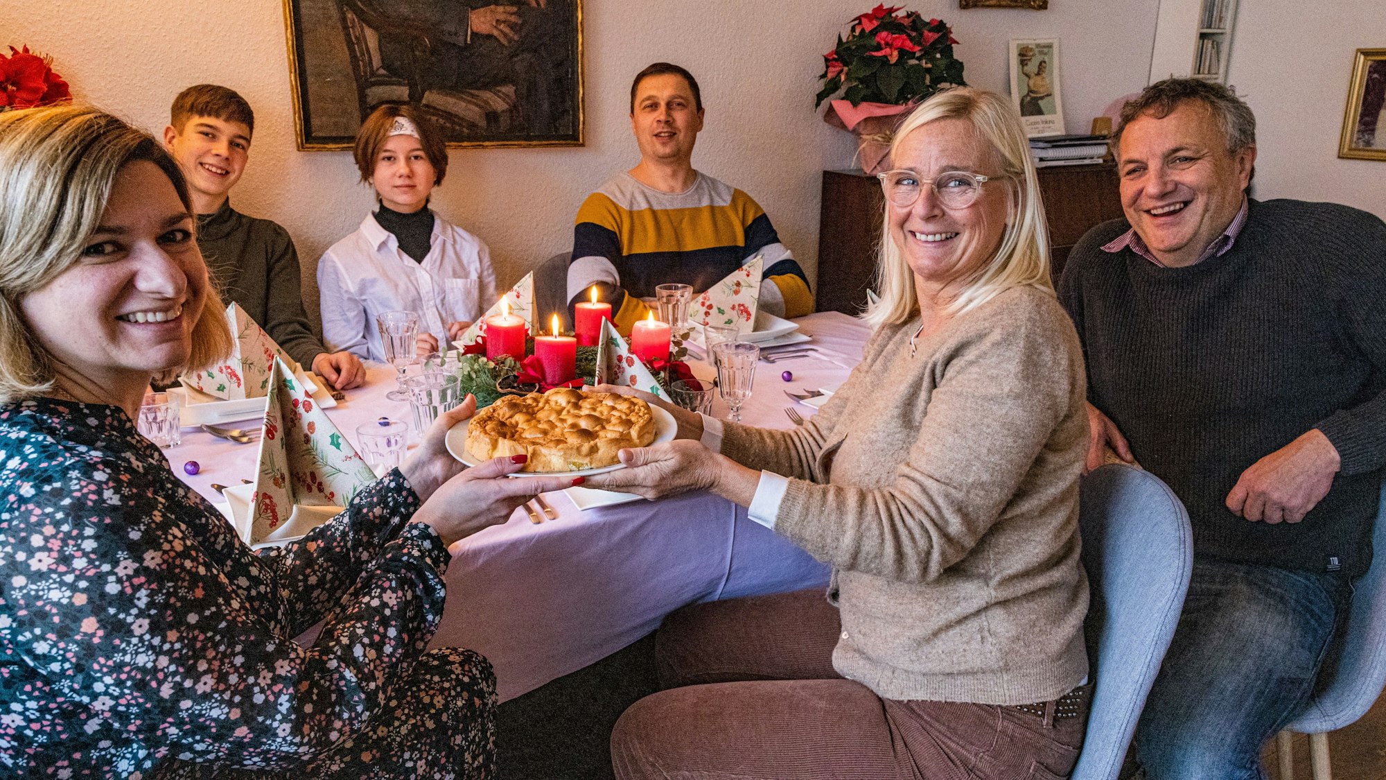 Schs Menschen sitzen gemeinsam an einem Esstisch und blicken in die Kamera.