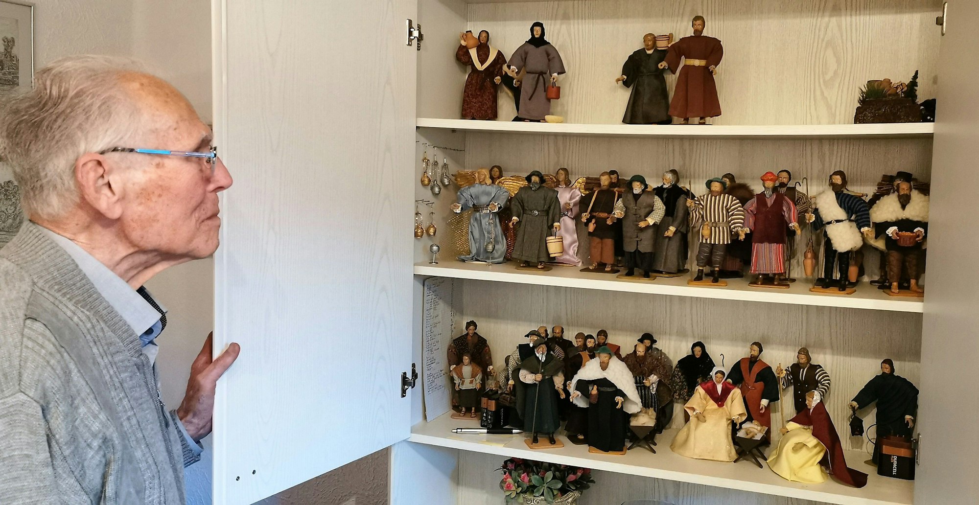 Ein älterer Mann steht vor dem offenen Regal. Im Regal befinden sich mehrere selbstgemachte Figuren.