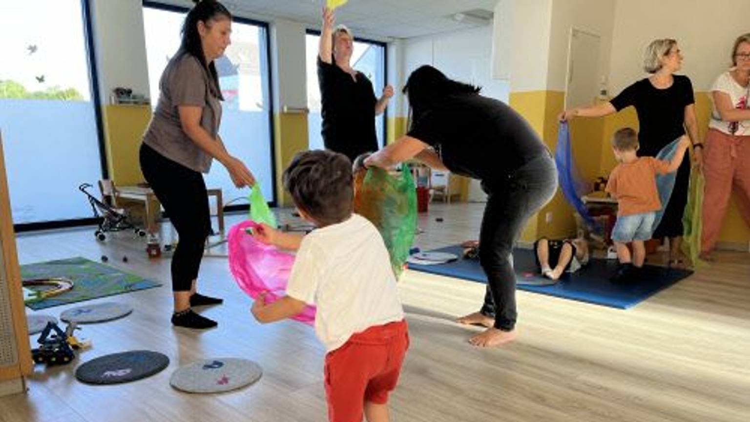 Mehrere Kinder und Erwachsene spielen in einem Raum mit Schwungtüchern.