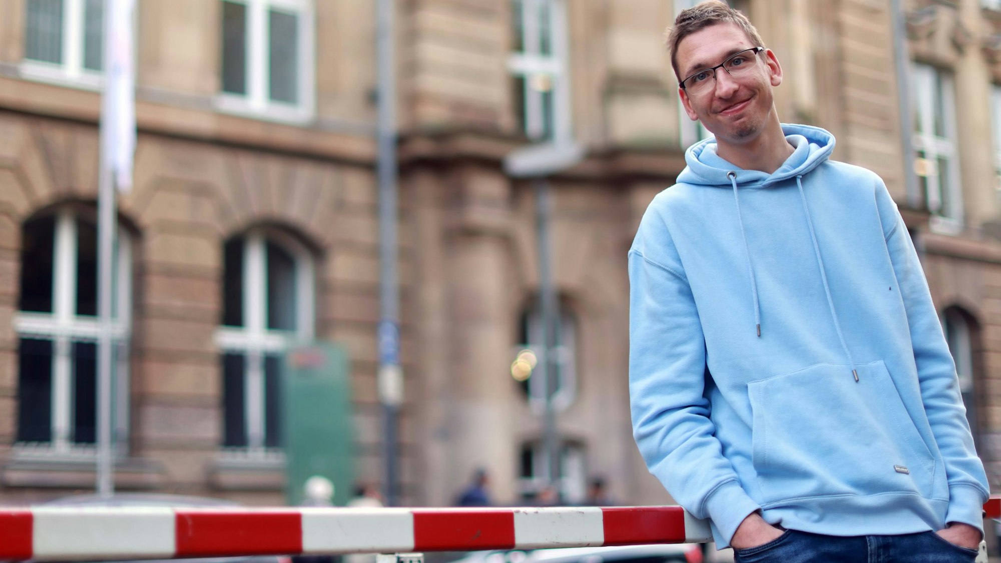 Kommunikative Kompetenz, Ideen und Erfahrung bringt Florian Lintz (32) in seinen Lehrauftrag ein – unter anderem. Er steht entspannt in einem hellblauen Sweatshirt vor dem Lehrgebäude am Ubierring.