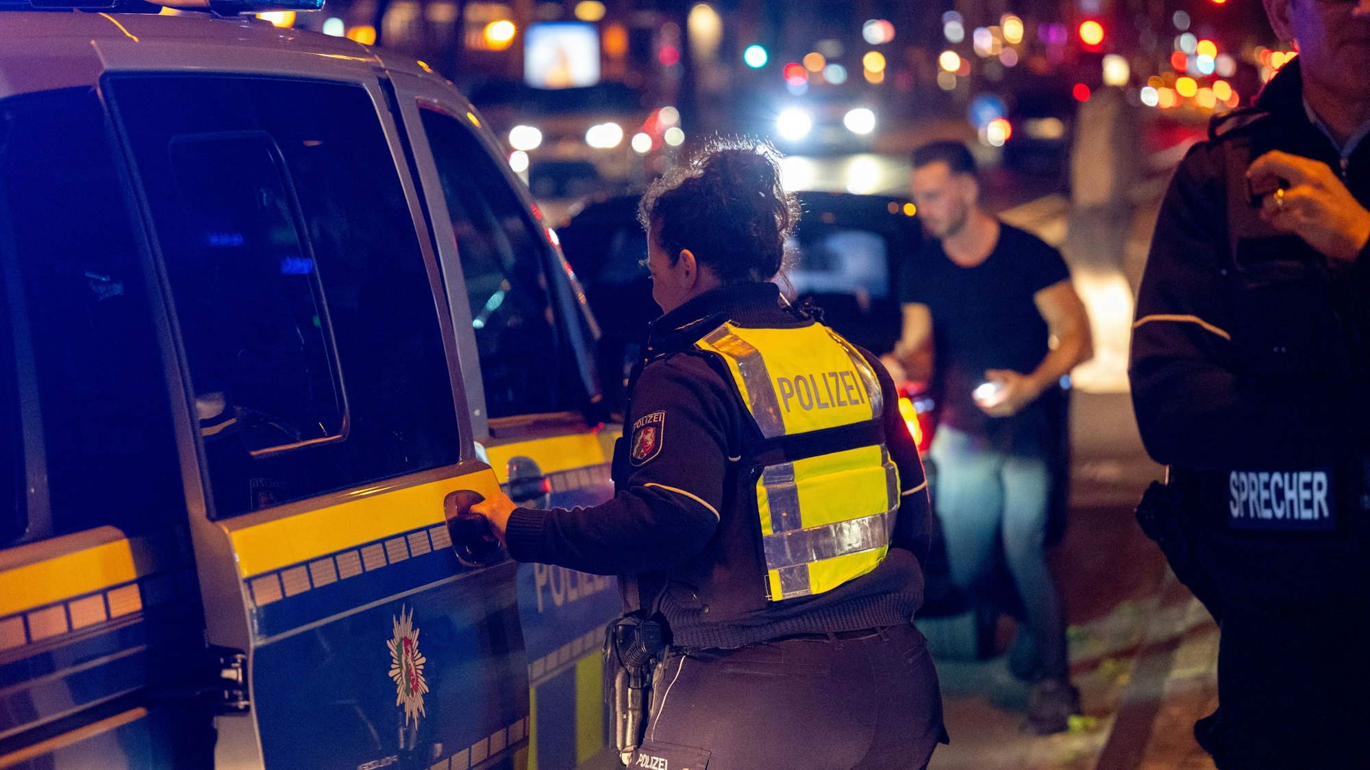 Ein Polizeiwagen steht auf einer Straße. Eine Polizistin steht an dem Wagen.