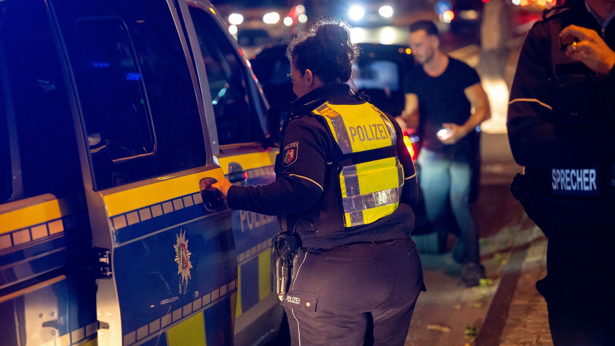 Die Polizei im Einsatz bei Nacht. Eine Polizistin schiebt die Tür eines Einsatzwagens zu.