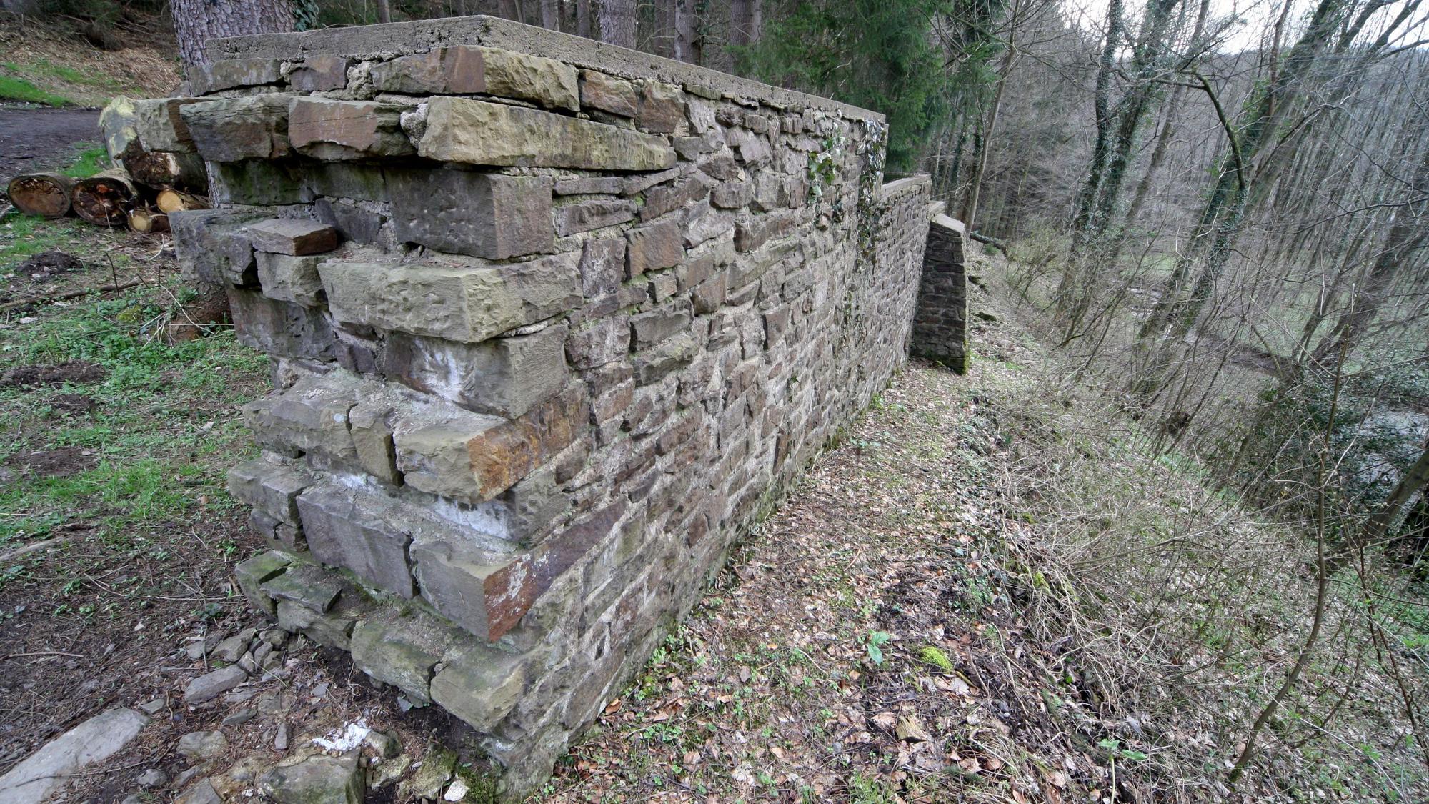 Eine Bruchsteinmauer steht in einem Wald.