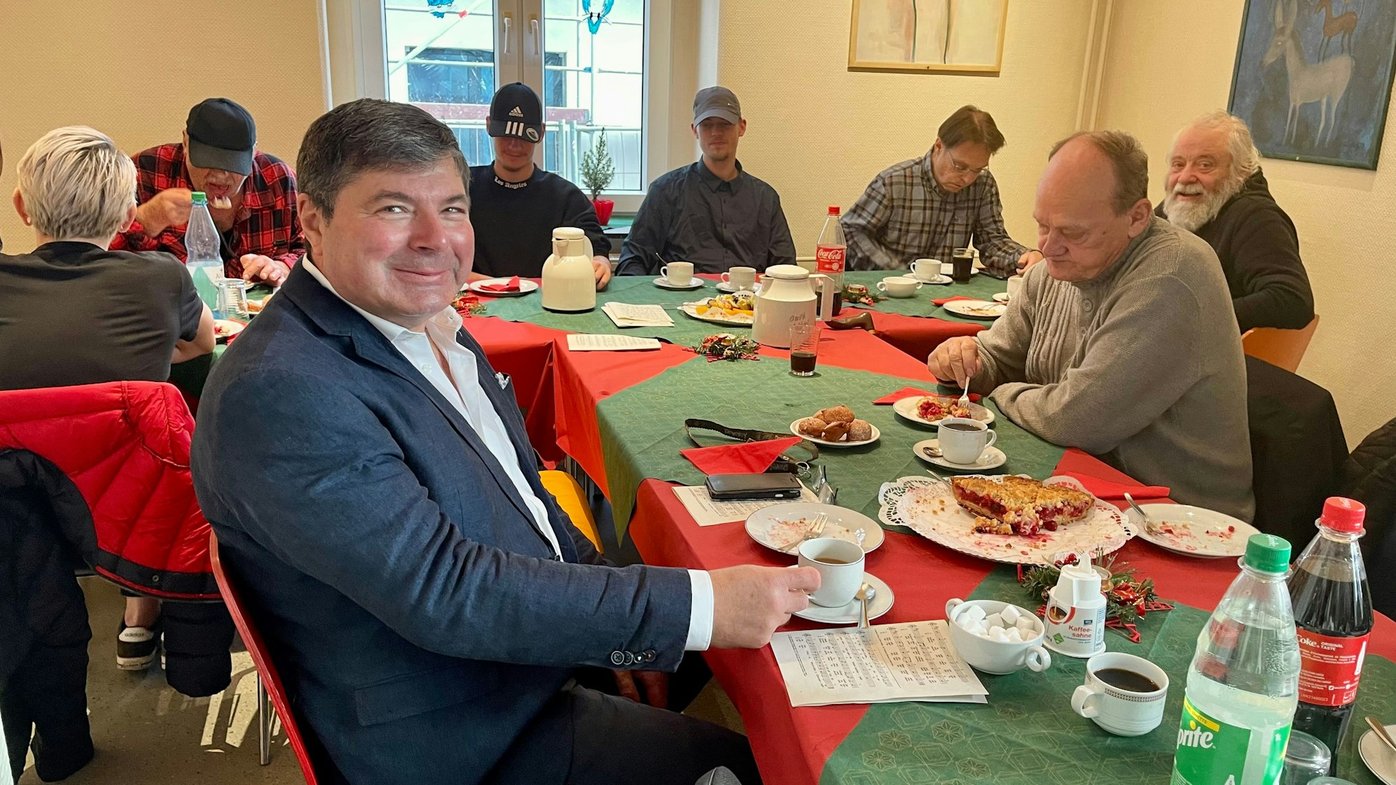 An einer langen Tafel sitzen mehrere Menschen vor Kaffeetassen und Kuchentellern.